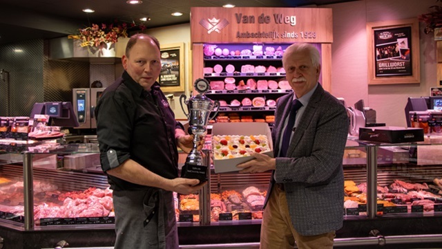 Slagerij van de Weg heeft prijs voor Nationaal Kampioen Hygiëne ontvangen, wethouder Henk Wessel overhandigt een taart aan de eigenaar en hij houdt trots de prijs vast